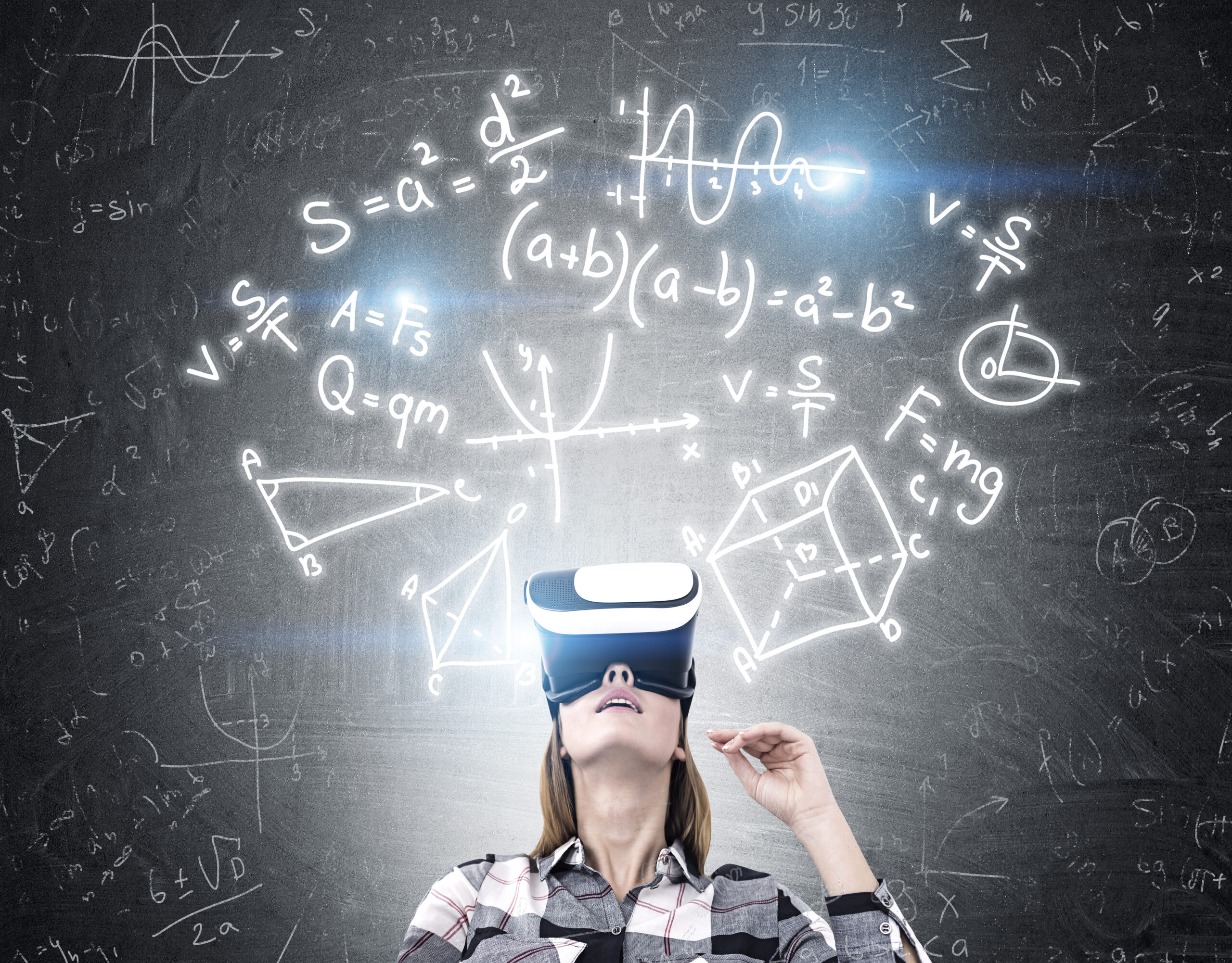 Portrait of a geeky girl wearing virtual reality glasses and looking upwards while standing near a blackboard with formulas
